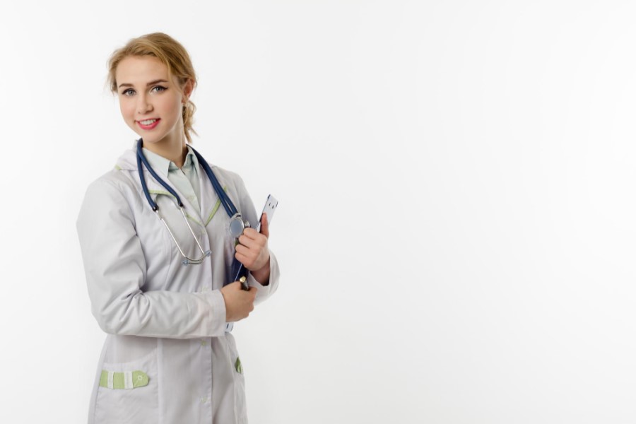 Młoda lekarka w kitlu i ze stetoskopem przewieszonym przez szyję. W ręce trzyma dokumenty.