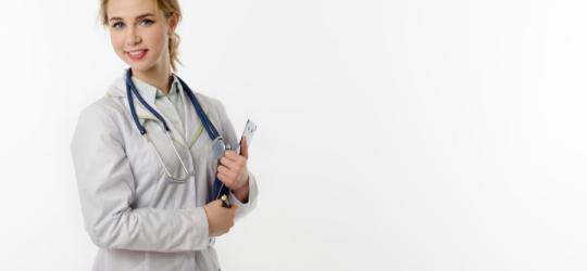 Młoda lekarka w kitlu i ze stetoskopem przewieszonym przez szyję. W ręce trzyma dokumenty.