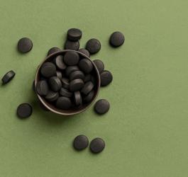 Tabletki węgla aktywowanego na zielonym tle.