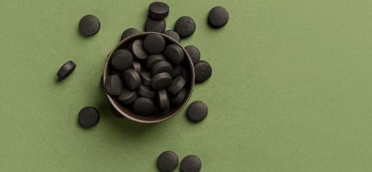 Tabletki węgla aktywowanego na zielonym tle.