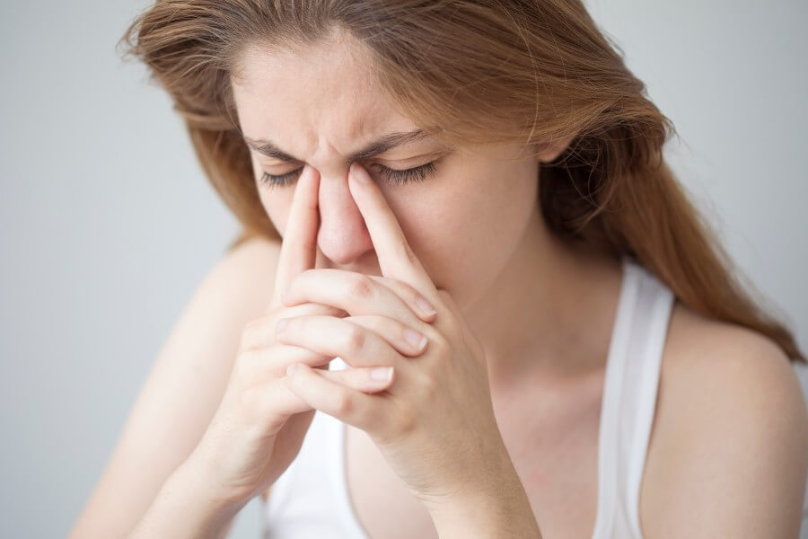 Kobieta trzyma się za nasadę nosa, cierpi na wirusowe zapalenie zatok.