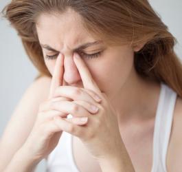 Kobieta trzyma się za nasadę nosa, cierpi na wirusowe zapalenie zatok.