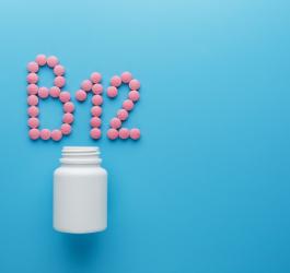 Różowe tabletki na niebieskim tle ułożone w napis B12, obok biała buteleczka.