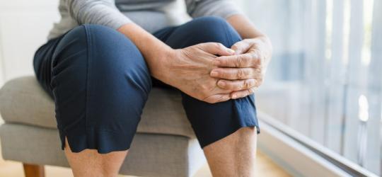 Starsza kobieta trzyma się za nogę, dokucza jej woda w kolanie.