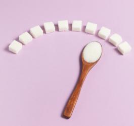 Różowe tło, na którym leżą kostki cukru i drewniana łyżeczka wypełniona cukrem.