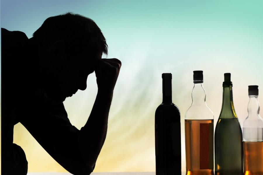 Zaciemniona twarz mężczyzny, który spogląda w stronę butelek z alkoholem.