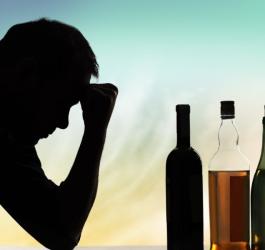 Zaciemniona twarz mężczyzny, który spogląda w stronę butelek z alkoholem.