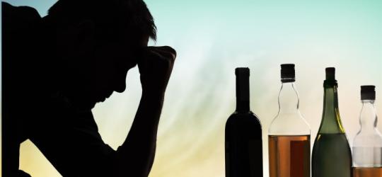 Zaciemniona twarz mężczyzny, który spogląda w stronę butelek z alkoholem.