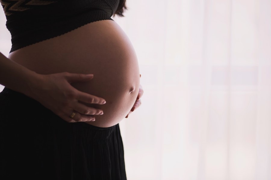 Kobieta w zaawansowanej ciąży, trzyma się dłońmi za widoczny brzuch.