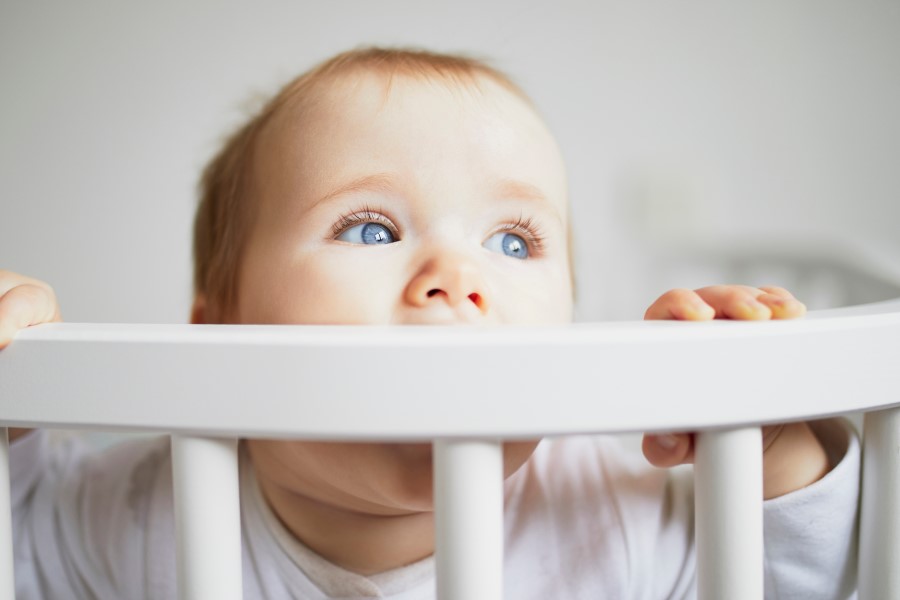 Niemowlę w drewnianym łóżeczku. Gryzie ramę łóżeczka, bo przechodzi ząbkowanie.