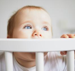 Niemowlę w drewnianym łóżeczku. Gryzie ramę łóżeczka, bo przechodzi ząbkowanie.