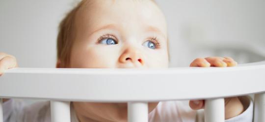 Niemowlę w drewnianym łóżeczku. Gryzie ramę łóżeczka, bo przechodzi ząbkowanie.