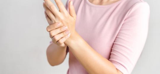 Kobieta trzyma się za jedną dłoń. Może cierpieć na zaburzenia czucia.