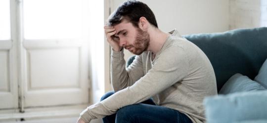 Zmartwiony z powodu zaburzeń erekcji mężczyzna siedzi na kanapie.