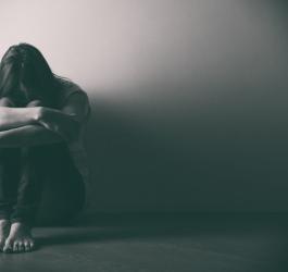 Zmartwiona kobieta siedzi na ziemi pod ścianą, trzyma głowę opartą o kolana.