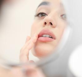 Kobieta ma w kącikach ust zajady, zmartwiona przegląda się w lustrze.