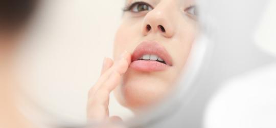 Kobieta ma w kącikach ust zajady, zmartwiona przegląda się w lustrze.