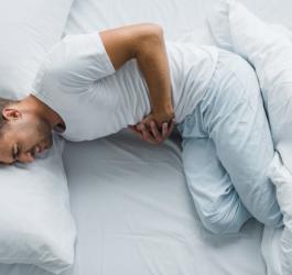 Mężczyzna leży w łóżku, boli go brzuch z powodu zapalenia błony śluzowej żoładka.