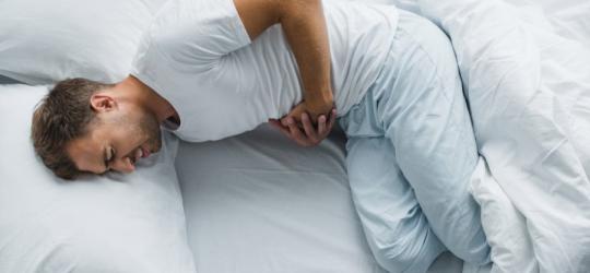 Mężczyzna leży w łóżku, boli go brzuch z powodu zapalenia błony śluzowej żoładka.