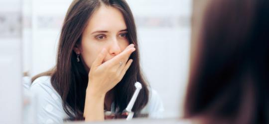 Kobieta przerywa szczotkowanie zębów z powodu bólu wywołanego zapaleniem dziąsła.