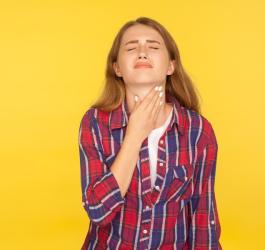 Kobieta chwyta się za szyję, cierpi na zapalenie przełyku, które powoduje dotkliwy ból.