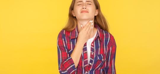 Kobieta chwyta się za szyję, cierpi na zapalenie przełyku, które powoduje dotkliwy ból.