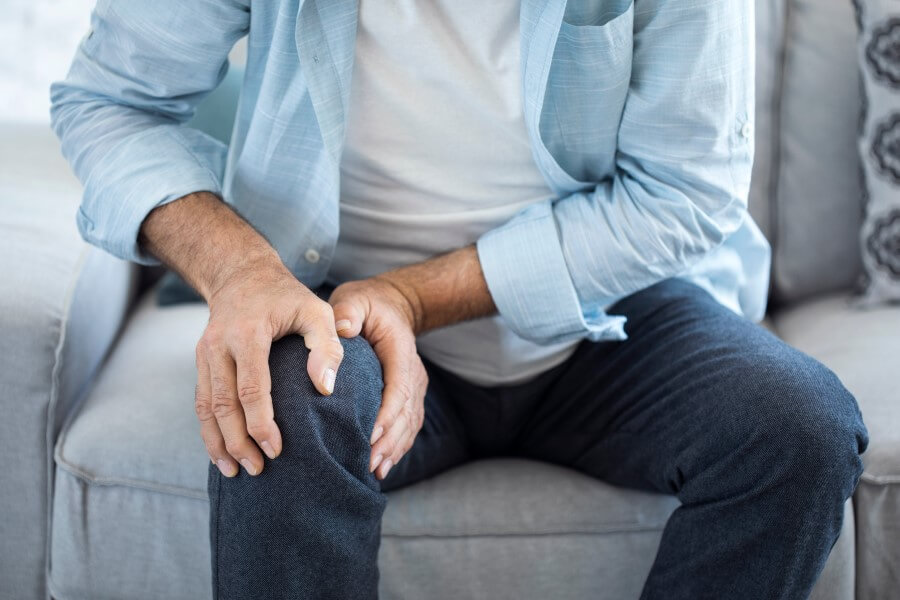 Mężczyzna trzyma się za kolano, które boli z powodu występującego zapalenia stawu kolanowego.