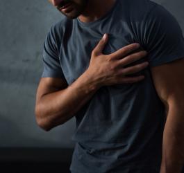 Mężczyzna trzyma dłoń na klatce piersiowej, może zmagać się z zapaleniem wsierdzia.