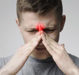 Mężczyzna trzyma się dłońmi za nasadę nosa, dokucza mu zapalenie zatok.