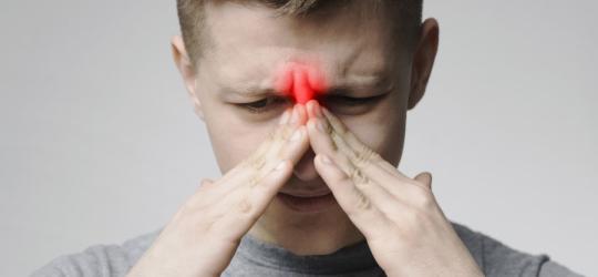 Mężczyzna trzyma się dłońmi za nasadę nosa, dokucza mu zapalenie zatok.