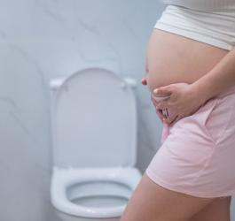Ciężarna kobieta stoi obok toalety, dokucza jej problem zaparć w ciąży.