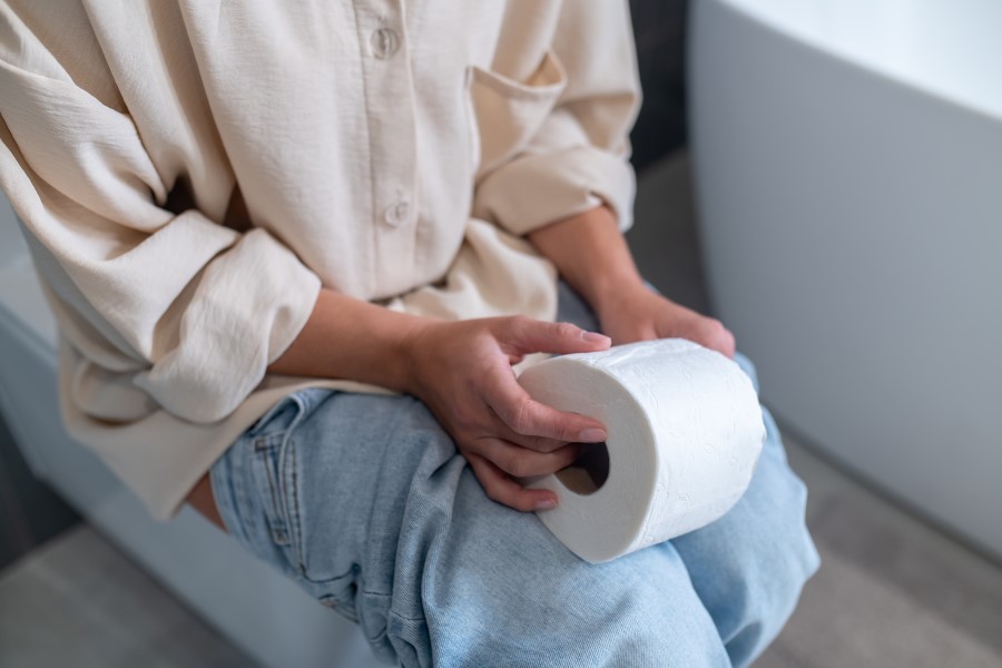 Kobieta siedzi na toalecie, trzyma w dłoniach papier toaletowy. Dokuczają jej zaparcia.