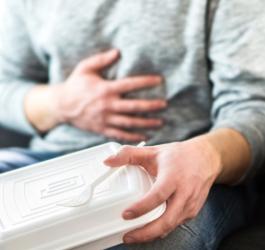 Mężczyzna trzyma w ręce pudełko po jedzeniu na wynos, boli go brzuch z powodu zatrucia pokarmowego.