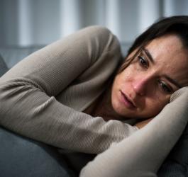 Kobieta leży na kanapie, wygląda na zmęczoną i zmartwioną.