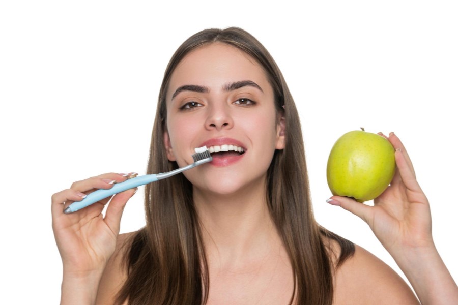 Kobieta trzyma w dłoni szczoteczkę do zębów i zielone jabłko.