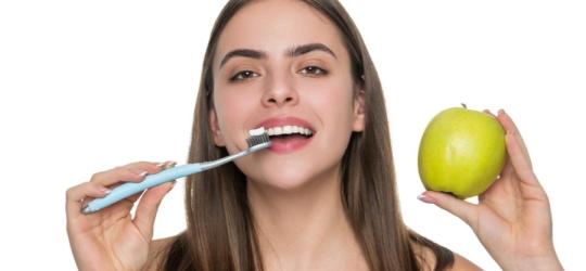 Kobieta trzyma w dłoni szczoteczkę do zębów i zielone jabłko.