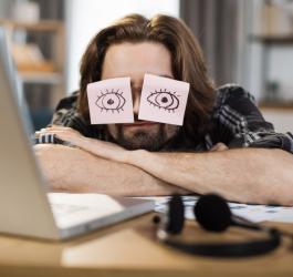 Przemęczony mężczyzna przysypia na biurku przed otwartym laptopem.