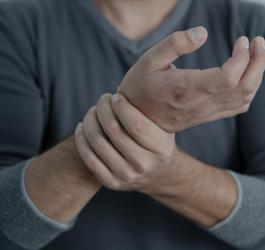 Mężczyzna trzyma się dłonią za nadgarstek drugiej ręki.