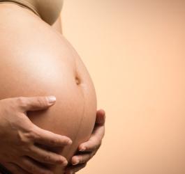 Kobieta trzyma się dłońmi za ciążowy brzuch.