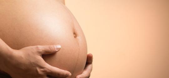 Kobieta trzyma się dłońmi za ciążowy brzuch.