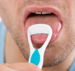 Mężczyzna usuwa nalot na języku przy pomocy specjalnej szczoteczki.