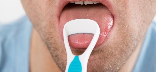 Mężczyzna usuwa nalot na języku przy pomocy specjalnej szczoteczki.