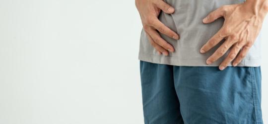 Mężczyzna trzyma się za podbrzusze, odczuwa dolegliwości spowodowane żylakami powrózka nasiennego.